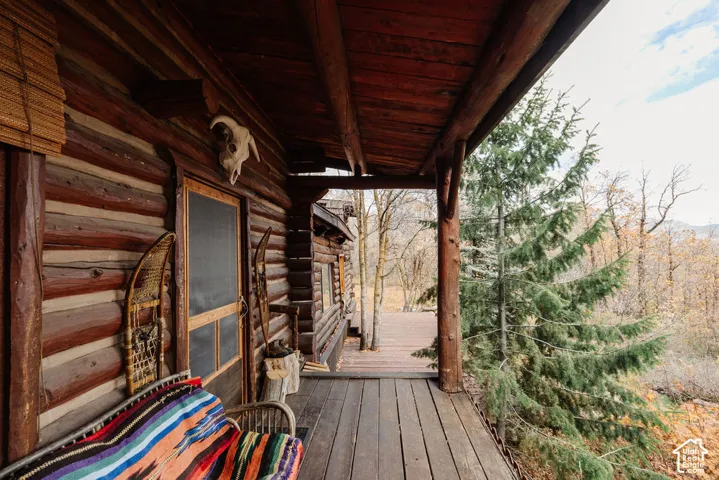 Covered log porch featuring structural timber support posts, horizontal log wall construction, and wood-plank decking
