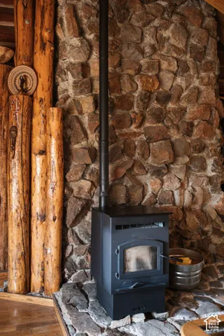 Full-height stone hearth featuring a vertical metal stove, rustic log-style vertical timbers, and a raised stone floor platform