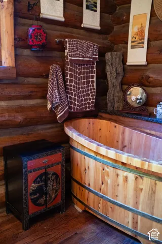Hand-hewn log walls, custom-crafted cedar soaking tub with metallic banding, and dark stone surface ledge