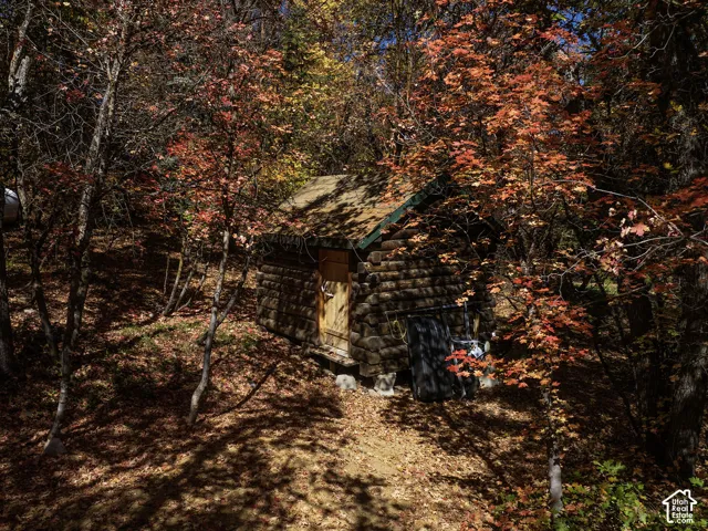 Rustic log cabin featuring stacked-timber construction, an asphalt shingle roof, and a wood-paneled door, situated within a wooded landscape