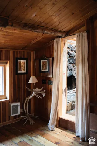 Natural wood-paneled walls and ceiling featuring exposed timber beams, wide-plank wood flooring, and a stone-clad exterior element visible through the doorway