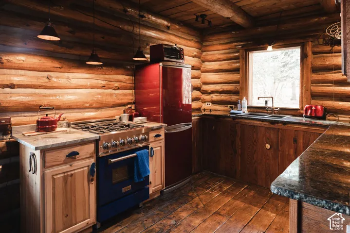 Rustic kitchen featuring exposed log walls, natural wood plank flooring, stone-finish countertops, custom wooden cabinetry, and industrial-style pendant lighting
