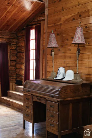 Exposed log walls, horizontal wood-plank wall paneling, vaulted ceiling with wood-plank finish, multi-pane window, and stepped wood flooring