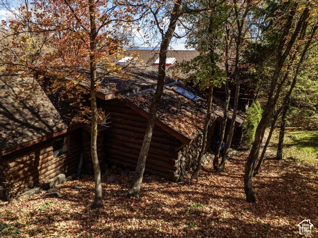 Log cabin exterior featuring horizontal timber walls, stone masonry accents, an asphalt shingle roof, and multiple skylights
