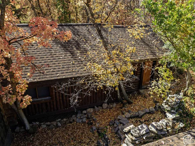 Log cabin exterior featuring stacked log siding, composition shingle roofing, and a natural stone retaining wall