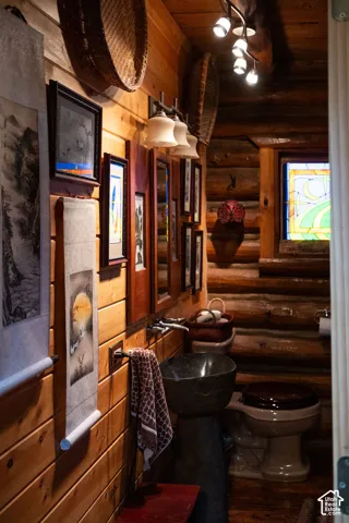 Interior space featuring exposed log walls, a pedestal stone-composite sink, stained glass window, and multi-directional track lighting