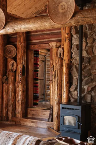 Log wall construction featuring exposed timber support beams, natural stone masonry fireplace surround, wood-finish flooring, and a free-standing black metal stove