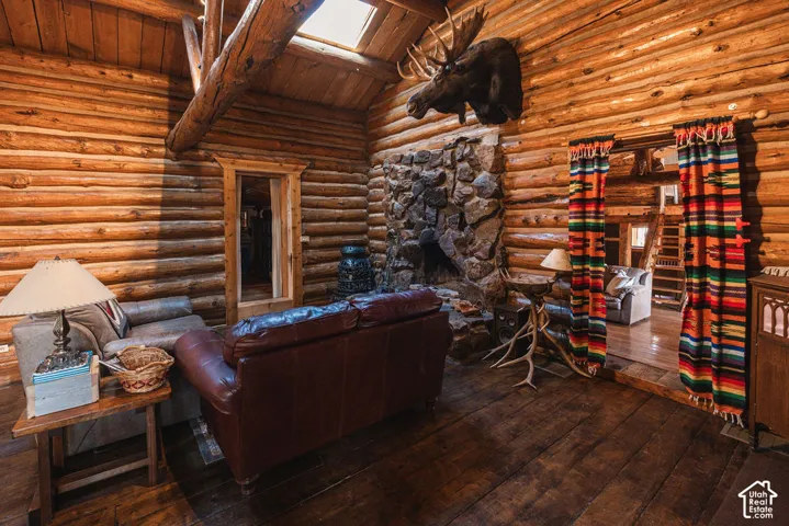 Living area featuring exposed log walls, vaulted ceilings with exposed timber beams, a floor-to-ceiling stone fireplace, and a skylight