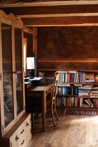 Exposed wood ceiling beams, dark stained wood paneling, built-in open bookshelves, wood-finish flooring, and a floor-to-ceiling built-in wood cabinet with glass door insets