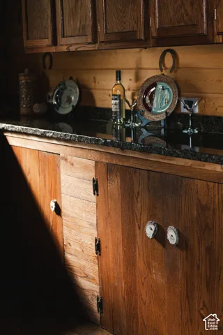 Custom wooden cabinetry featuring unique stone-slice hardware, dark stone countertop, and wood-paneled walls