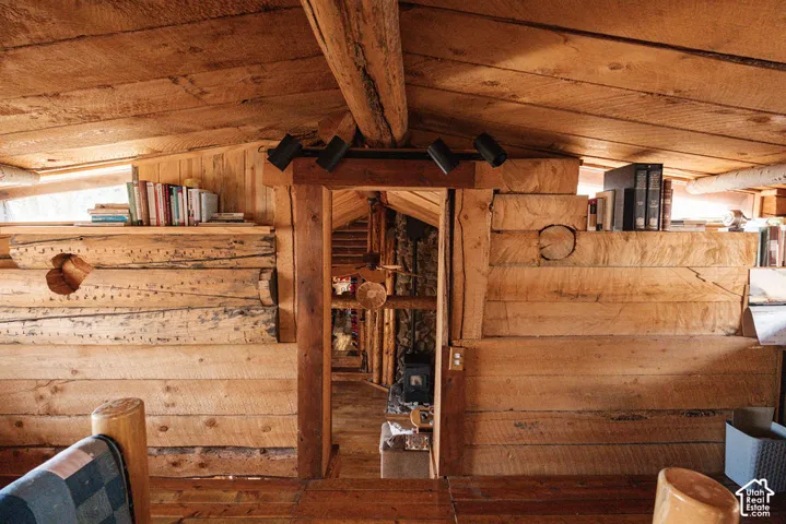 Rustic log construction featuring exposed timber ceiling beams, handcrafted stacked-log walls, integrated timber shelving, and adjustable track lighting