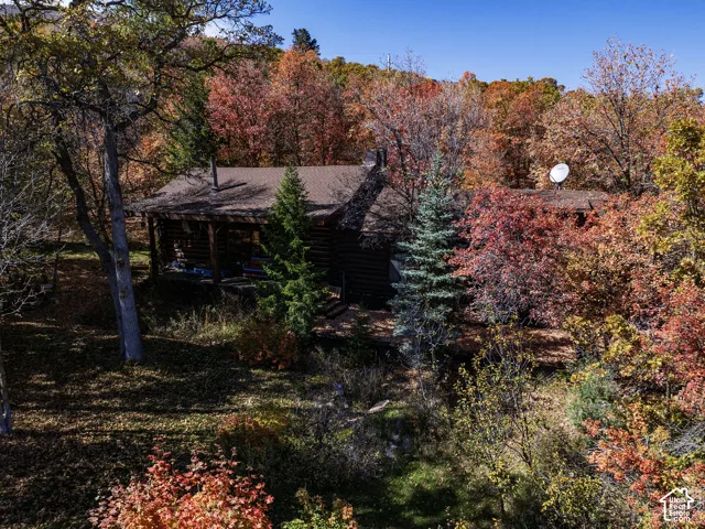 Log cabin exterior featuring a covered front porch, dark-stained timber construction, and a stone chimney, situated within a wooded lot