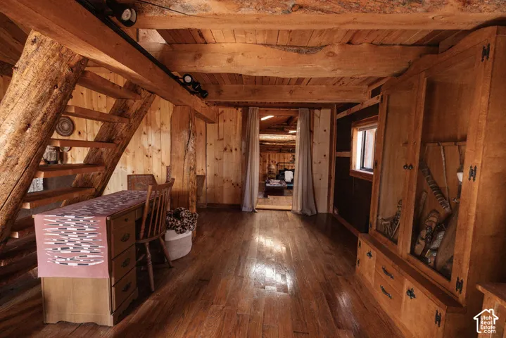 Exposed log beam ceiling, natural wood wall paneling, wide-plank wood-finish flooring, custom built-in cabinetry with glass-front shelving, and integrated wooden staircase