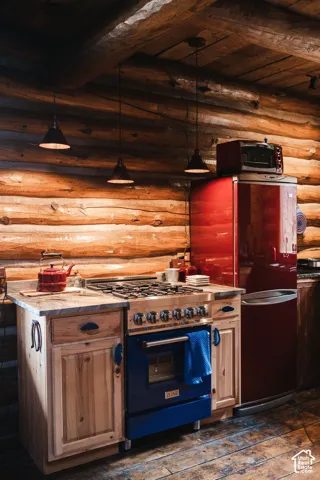 Kitchen featuring horizontal log walls, exposed timber ceiling beams, custom wood cabinetry, stone-finish countertops, and professional-grade gas range