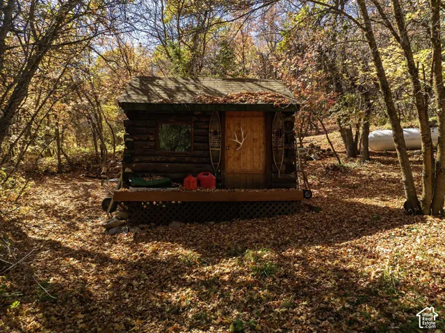 Log cabin structure featuring horizontal log exterior walls, a gabled roof, a wood-plank entry door, and an attached elevated wooden deck with lattice skirting
