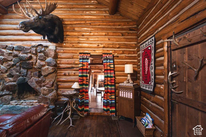 Interior featuring exposed log walls, natural wood ceiling beams, and a floor-to-ceiling stone fireplace