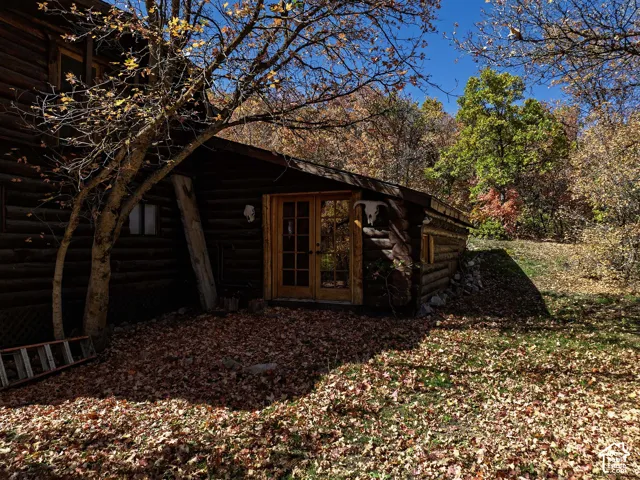 Log exterior residence featuring stacked timber construction, natural stone retaining wall, and wood-framed glass paneled doors