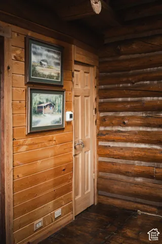 Rustic log walls paired with smooth wood paneling, solid wood six-panel door, and dark-toned wood flooring