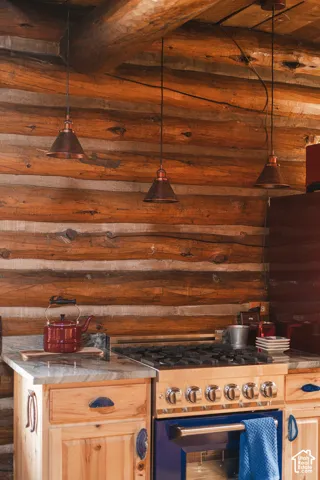Natural log walls, exposed log ceiling beam, stone-finish countertops, stainless steel professional-style gas range, and three copper-finish pendant lights