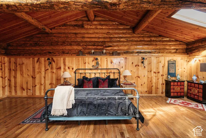Vaulted ceiling featuring exposed timber beams and stacked log walls, vertical wood-plank wall paneling, wood-finish flooring, and a large skylight