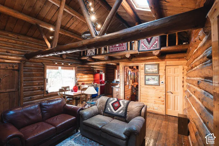 Exposed log walls, vaulted ceiling with heavy timber beams, loft space with wood railing, skylight, and wood-finish flooring