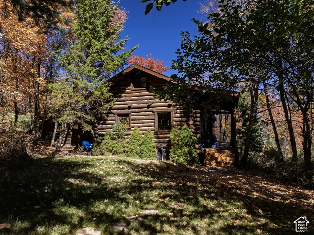 Log cabin exterior featuring horizontal timber construction, a gabled roof, an attached porch, and mature deciduous and coniferous trees