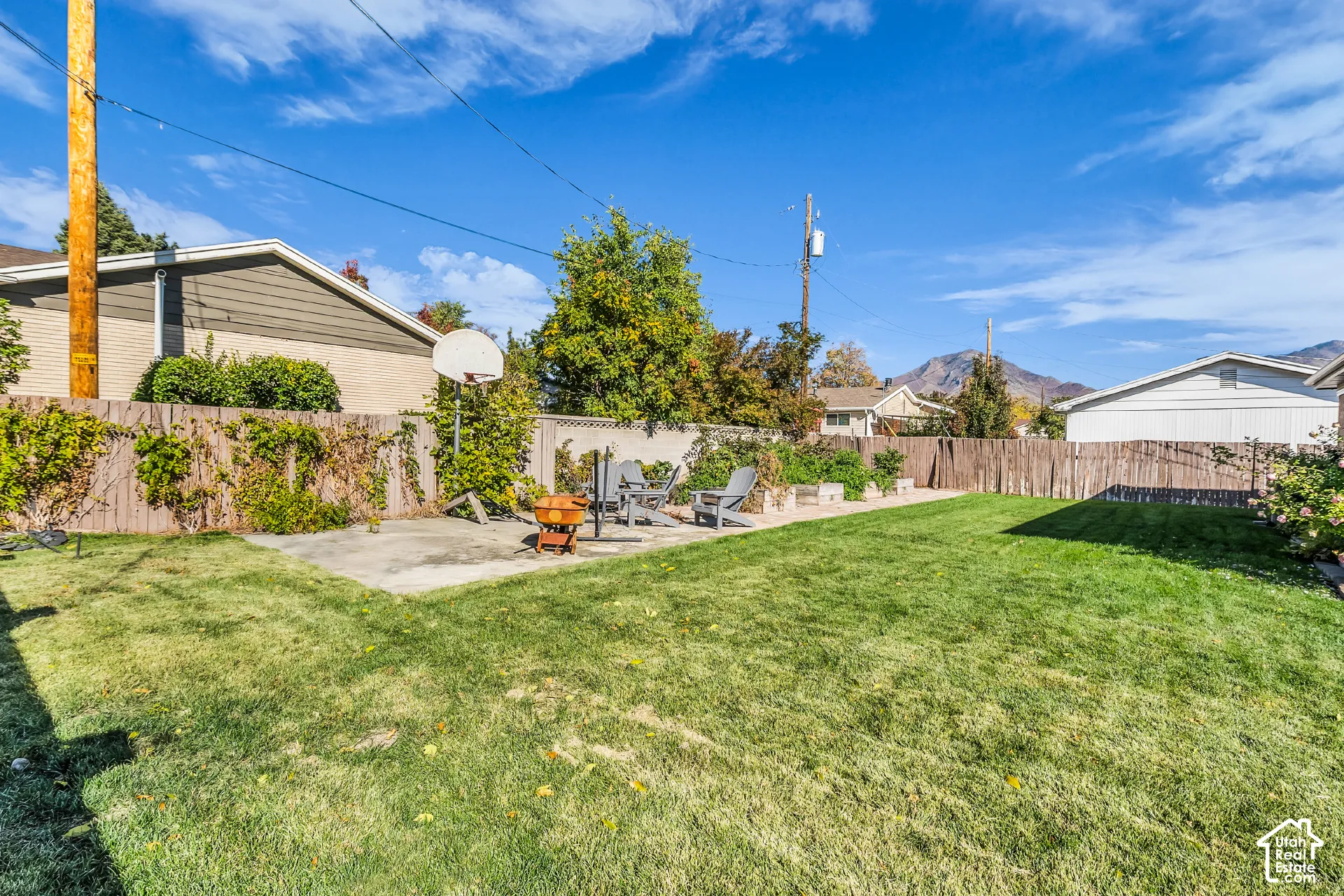 Spacious backyard featuring a manicured lawn, concrete patio, perimeter wood fencing, and mountain backdrop