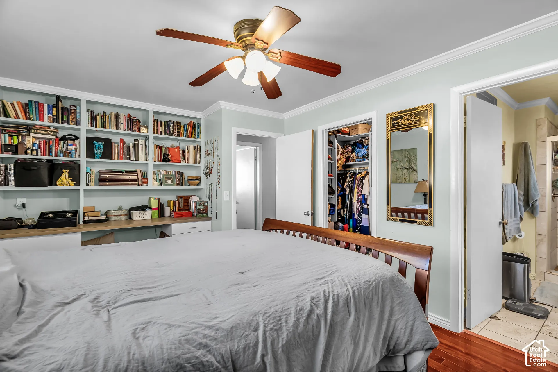 Built-in floor-to-ceiling wooden bookshelves with integrated desk, ceiling fan with light fixture, and hardwood flooring