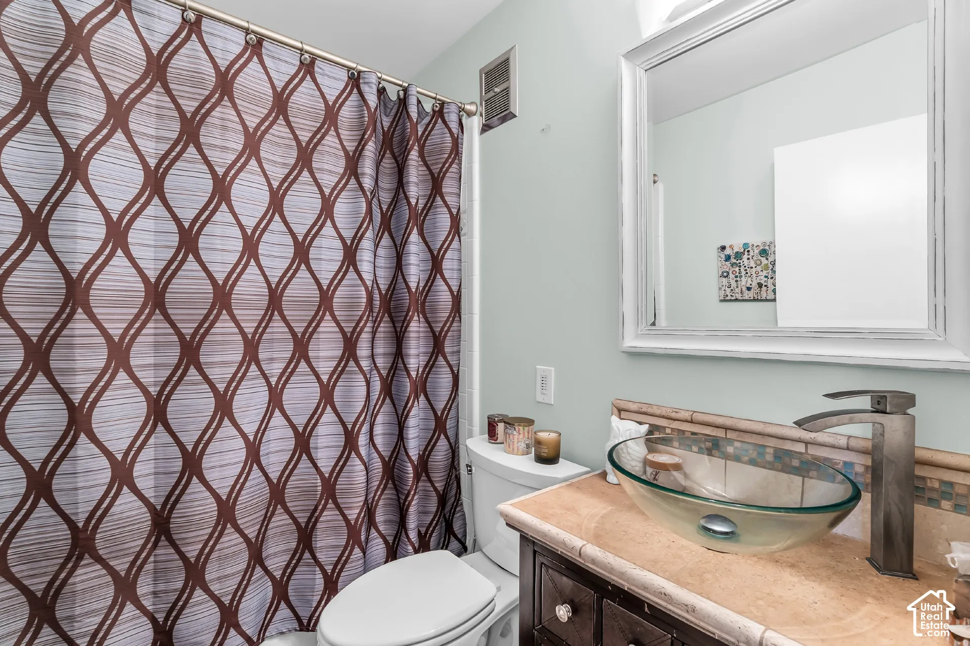 Bathroom vanity featuring a natural stone countertop, glass vessel sink, dark wood-finish cabinetry, and a wall-mounted framed mirror