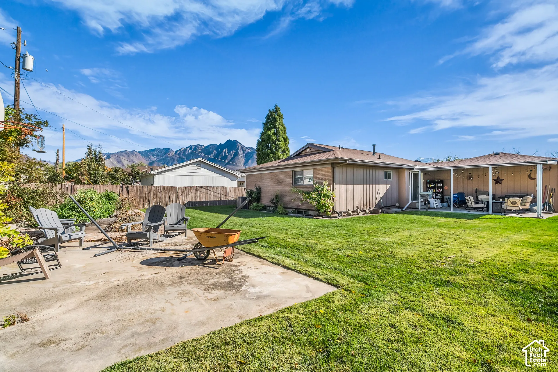 Expansive backyard featuring a concrete patio, covered porch area, wood-style fencing, and mountain backdrop