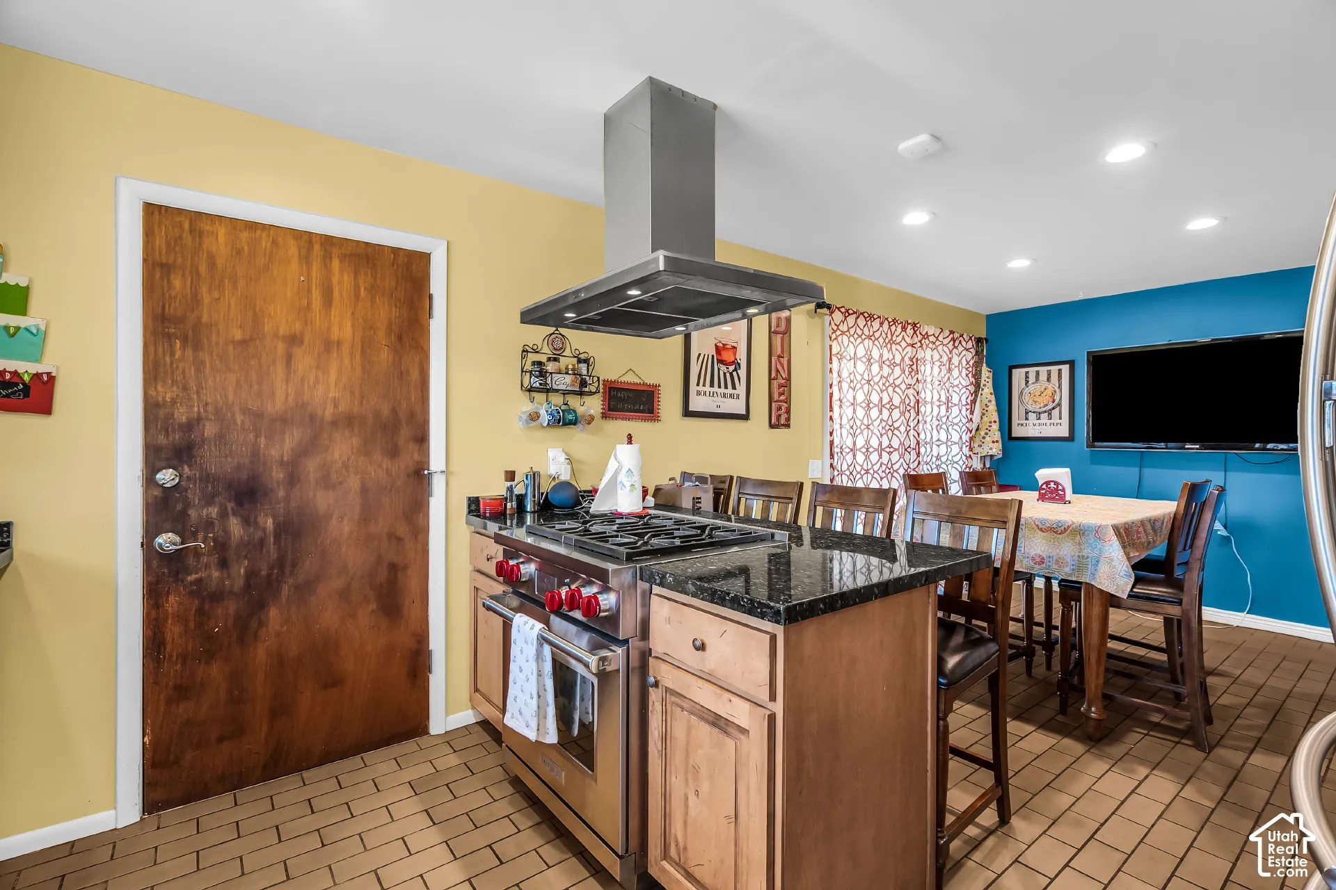 Kitchen island featuring a stone-surface countertop, stainless steel gas range, overhead stainless steel vent hood, and natural-finish wood cabinetry