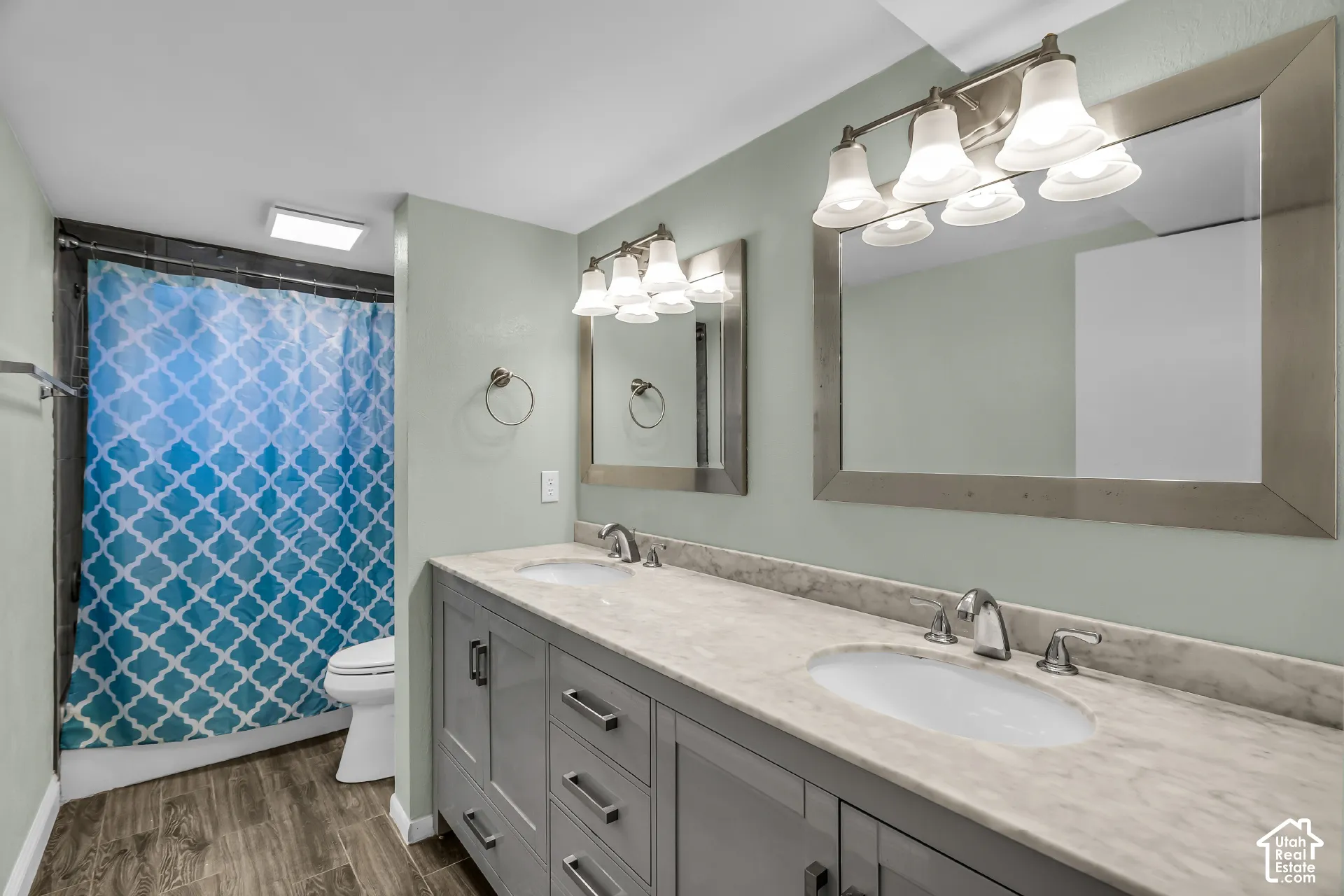 Double vanity featuring grey shaker-style cabinetry, stone-finish countertops with dual undermount sinks, wood-finish flooring, and framed wall mirrors