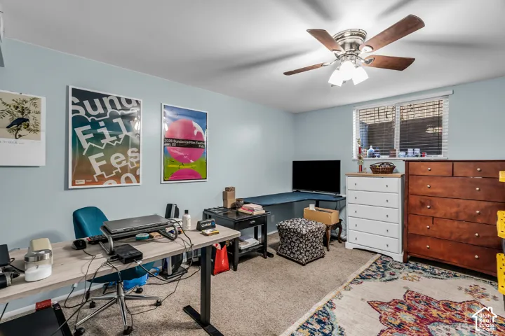 Room featuring neutral carpeting, a ceiling-mounted light fixture with a fan, and an integrated corner desk surface