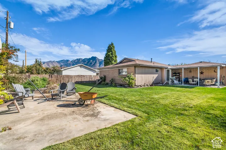 Expansive backyard featuring a concrete patio, covered porch area, wood-style fencing, and mountain backdrop