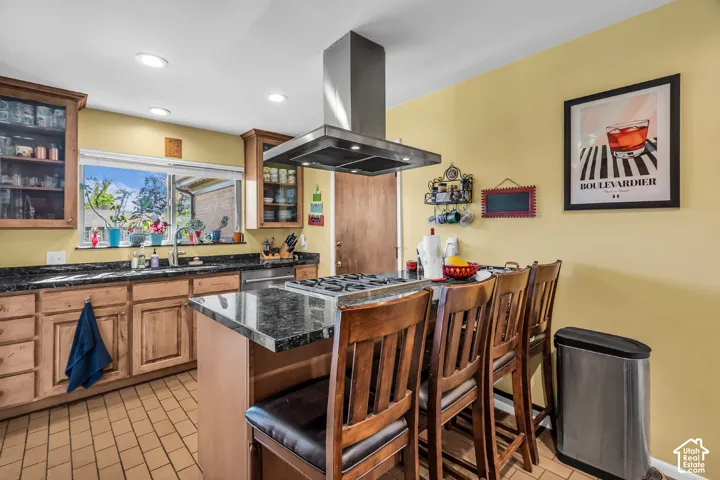 Kitchen featuring wood cabinetry, stone countertops, a center island with a built-in cooktop, a stainless steel chimney-style range hood, and recessed lighting