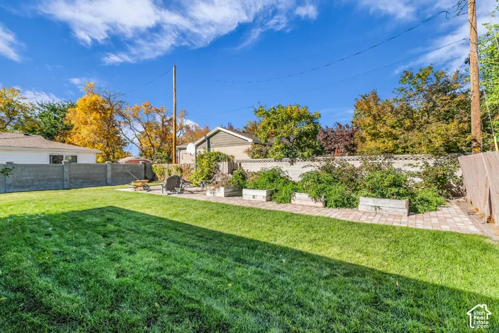 Rear yard featuring a manicured lawn, stone paver patio, raised garden beds, and masonry perimeter fencing
