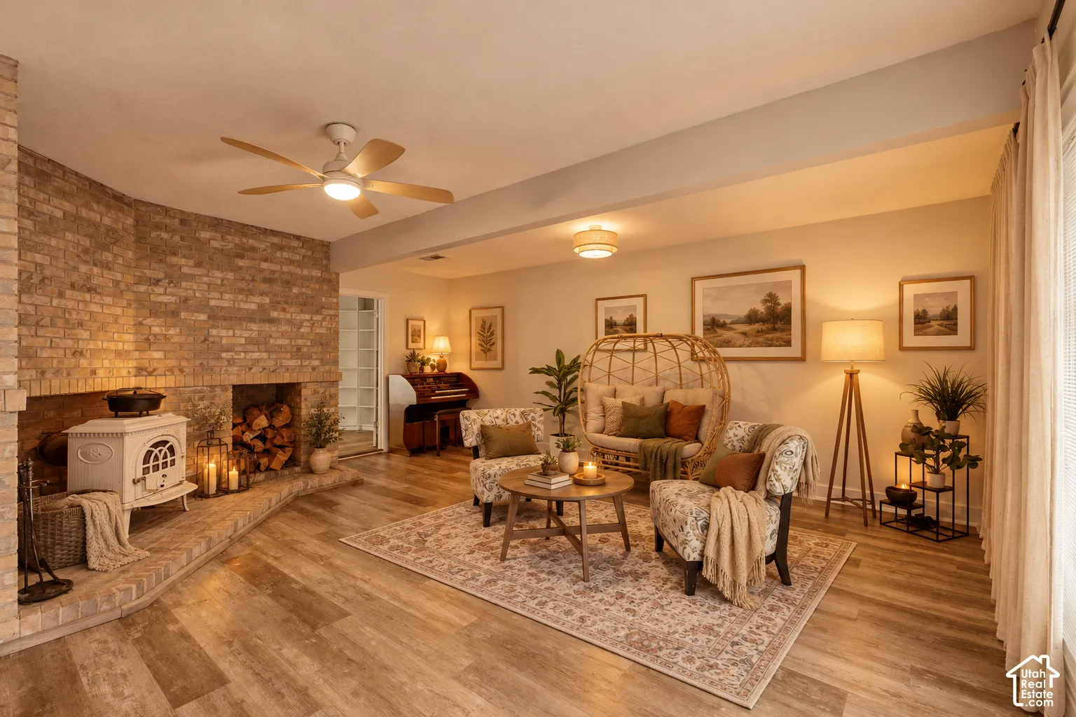 Brick fireplace surround with a freestanding stove, wood-finish flooring, and a ceiling fan with integrated lighting