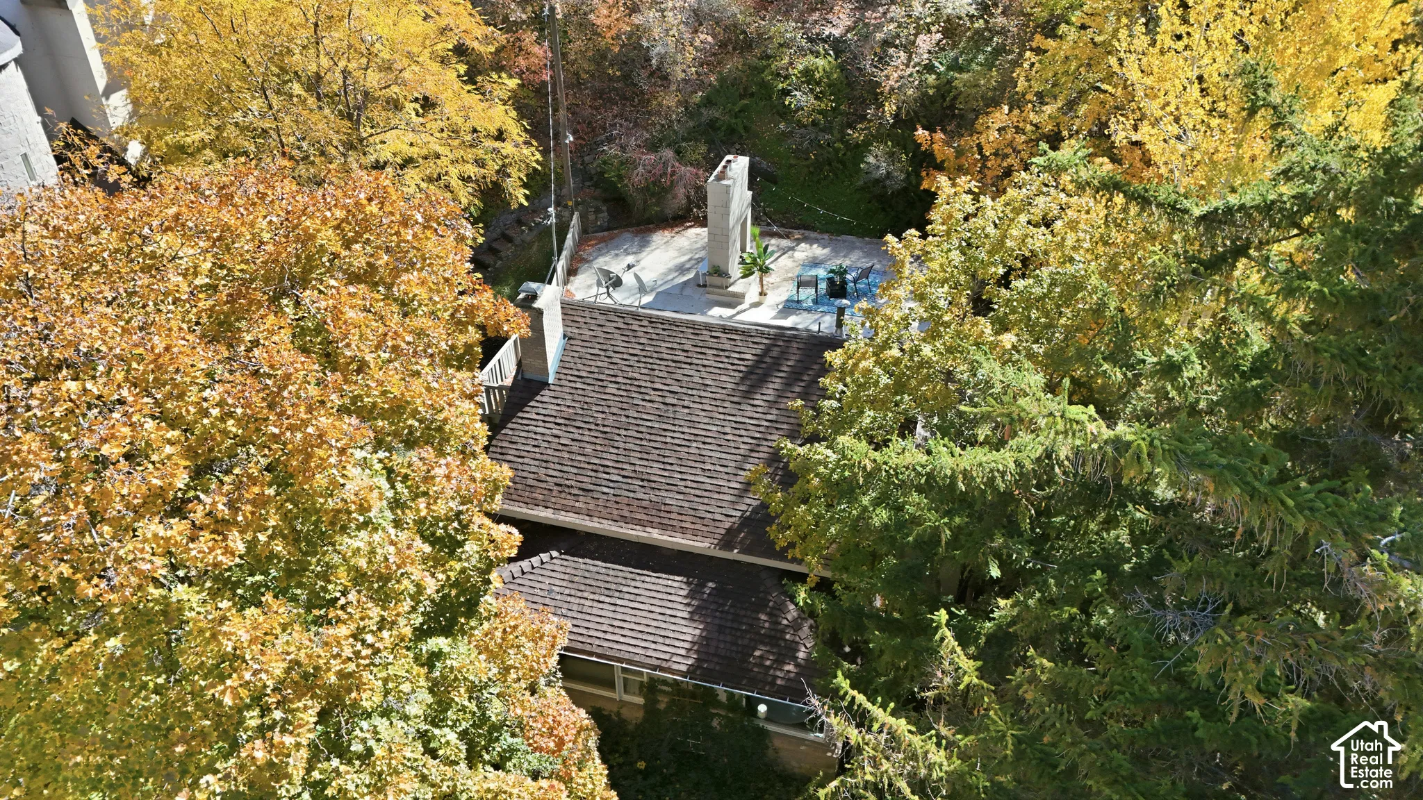 Aerial perspective featuring a multi-level asphalt shingle roof, a spacious concrete patio, and a tall stone-clad exterior fireplace