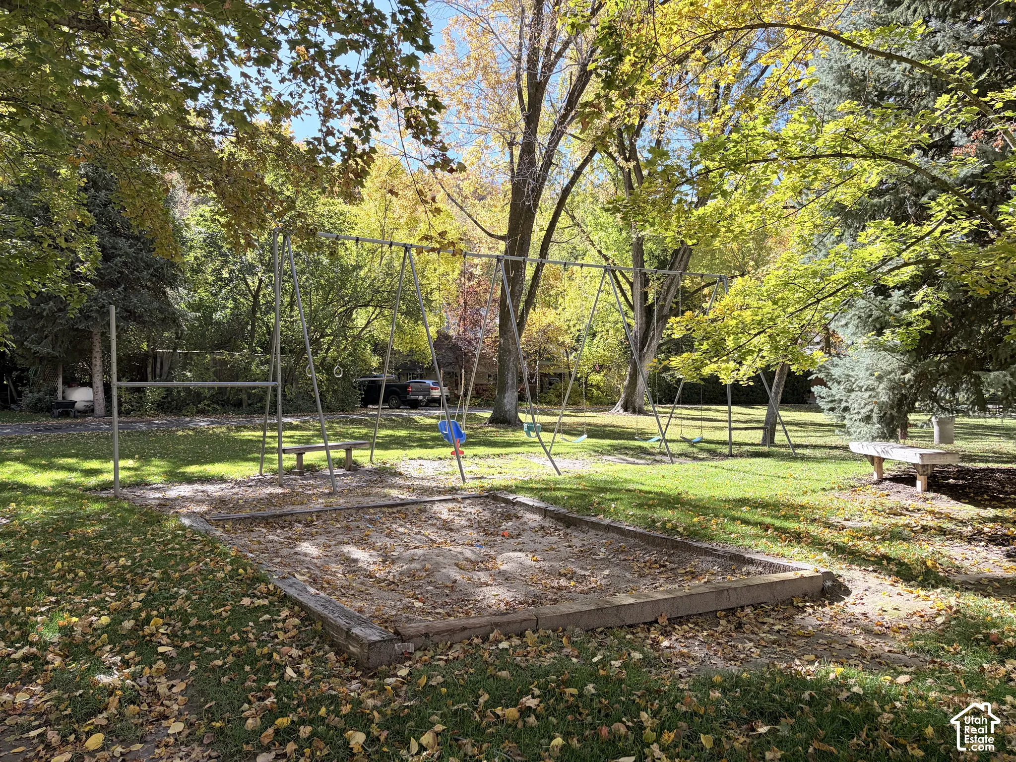 Expansive grounds featuring a metal swing set, timber-framed sandbox, stone benches, and mature trees