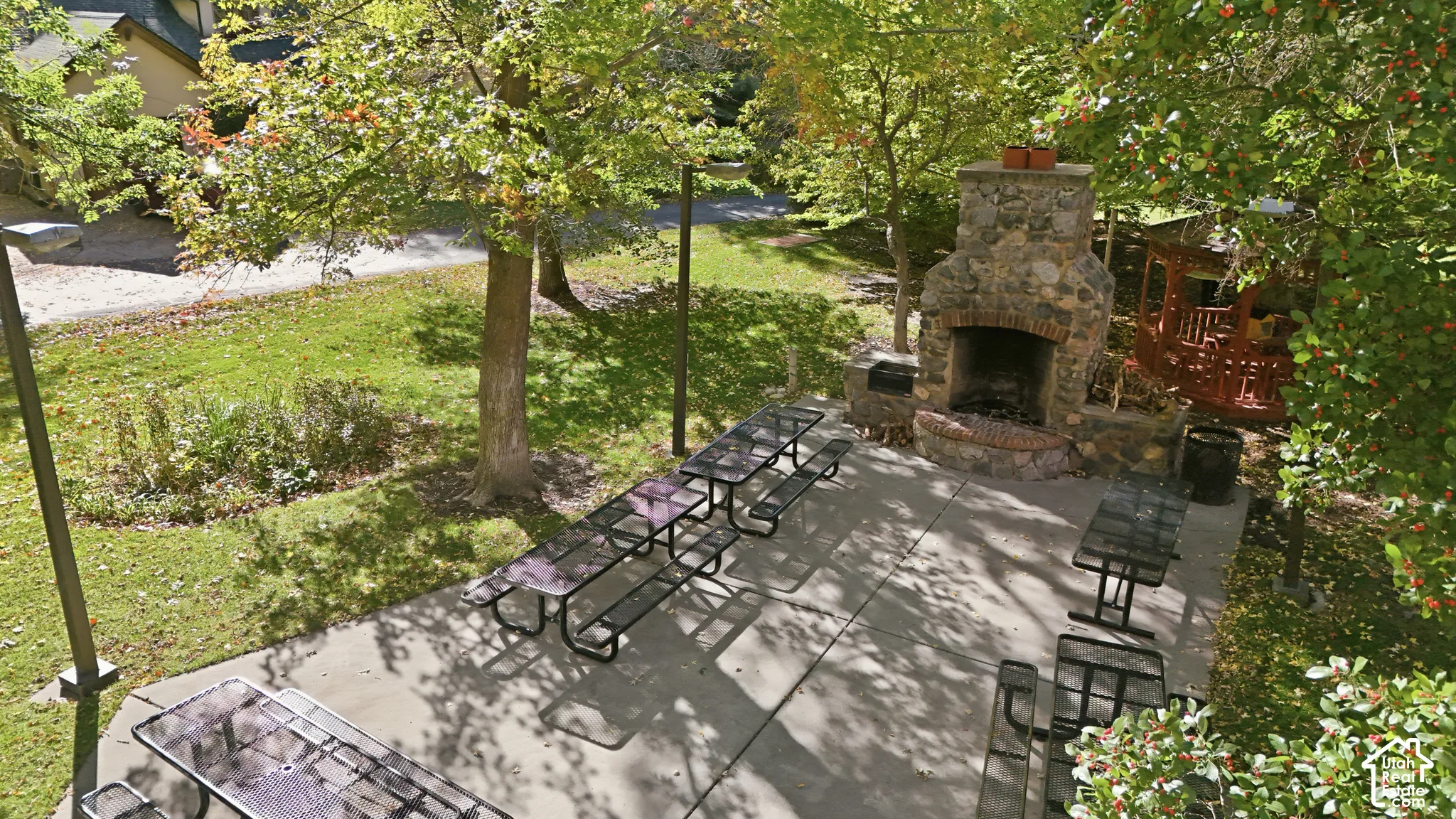 Concrete patio featuring a natural stone outdoor fireplace, a wooden gazebo, and post-mounted exterior lighting, plenty of seating, this is a community area