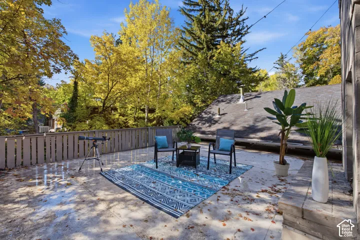 Upstair terrace deck featuring a stone fireplace, wood-slat fencing, and a natural, wooded mountain backdrop
