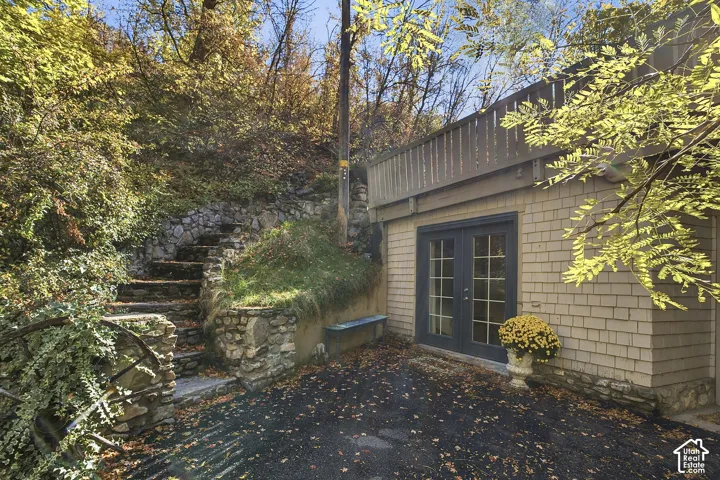 Exterior featuring shingle siding, double glass-panel doors, a wood-railing deck, and integrated stone landscaping steps