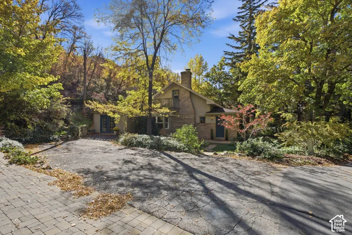 Multi-level exterior featuring a brick  facade, a paved driveway, an upper-level balcony, and a stone chimney