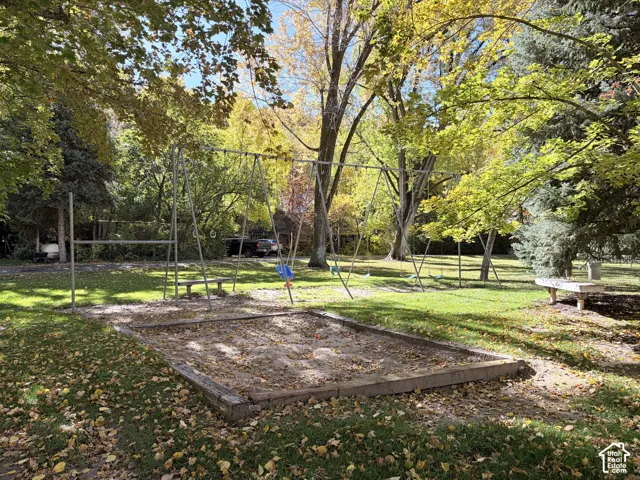 Expansive grounds featuring a metal swing set, timber-framed sandbox, stone benches, and mature trees