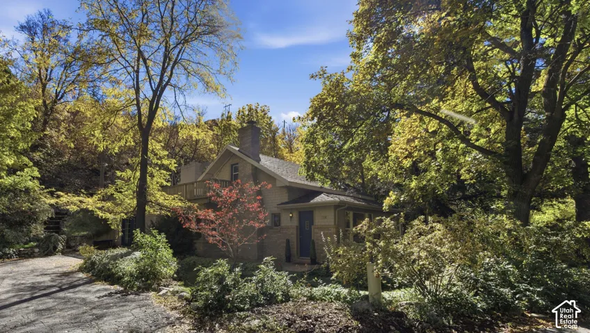 Two-story residence featuring brick exterior masonry, roofline, exterior balcony, stone-surround chimney, and a paved private drive