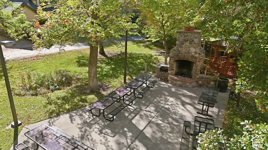 Concrete patio featuring a natural stone outdoor fireplace, a wooden gazebo, and post-mounted exterior lighting, plenty of seating, this is a community area