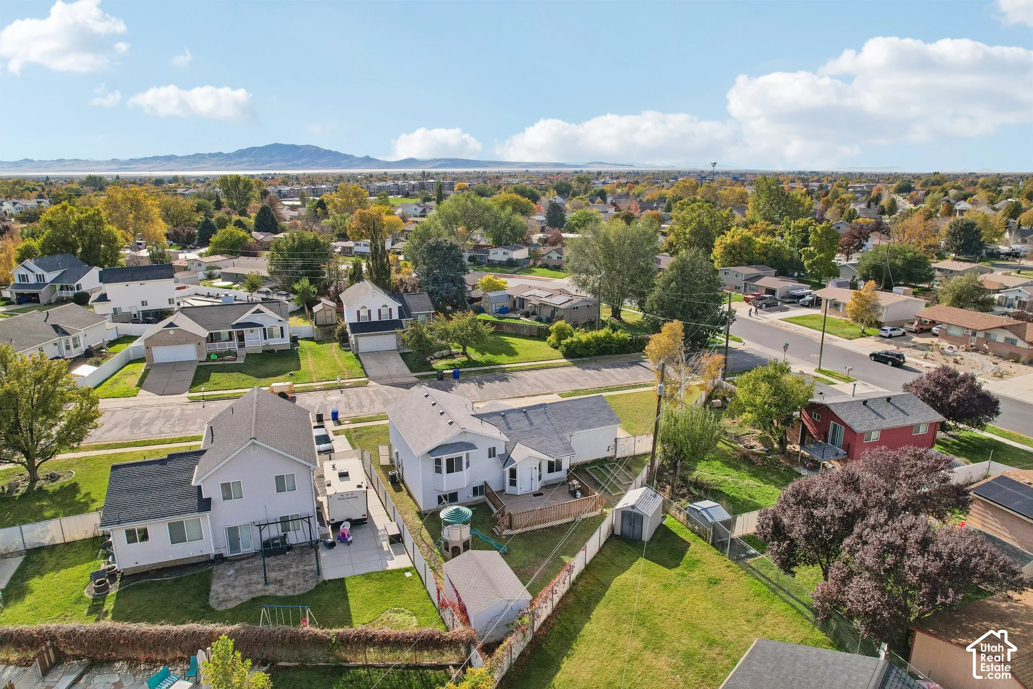 Aerial perspective featuring paved driveways, established landscaping, fenced perimeters, and a distant mountain backdrop