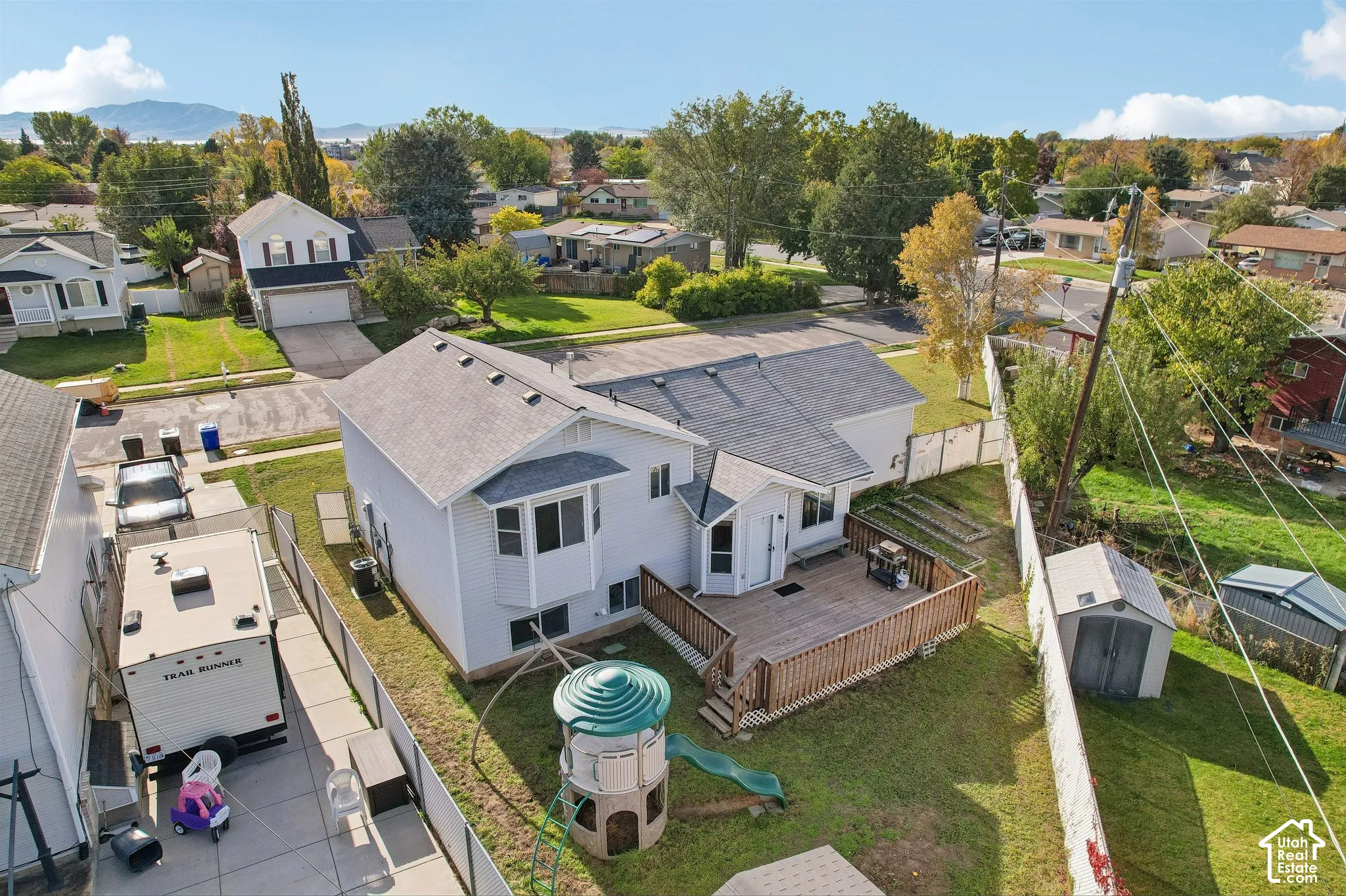 Aerial perspective of a detached residence featuring a wood deck, a fenced rear yard, a storage shed, and a side-yard concrete pad