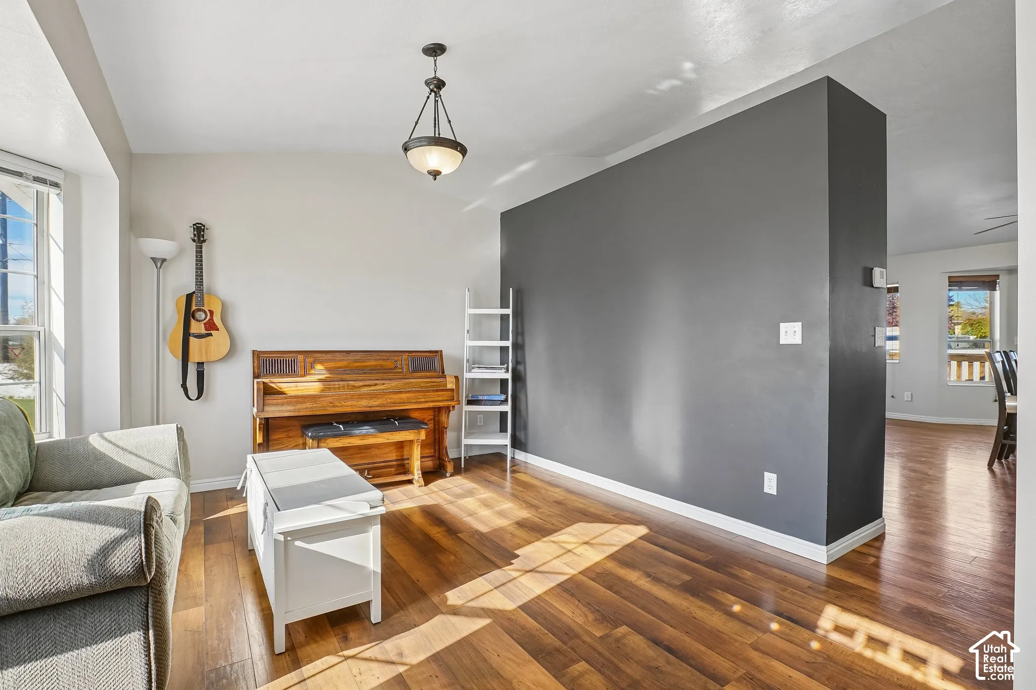 Living area featuring wood-finish flooring, a charcoal-toned accent wall, and a traditional pendant light fixture
