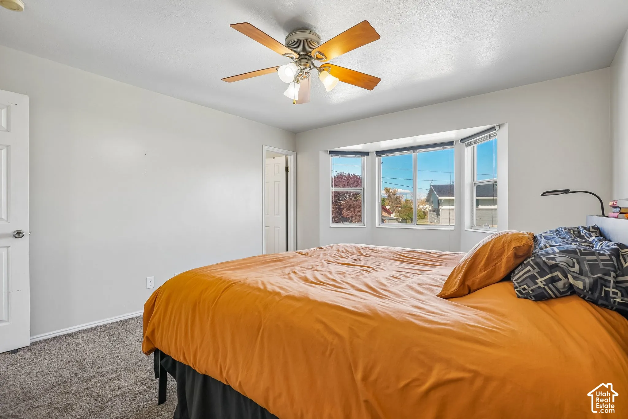 Room featuring a bay window, ceiling-mounted light fixture with a fan, and wall-to-wall carpeting